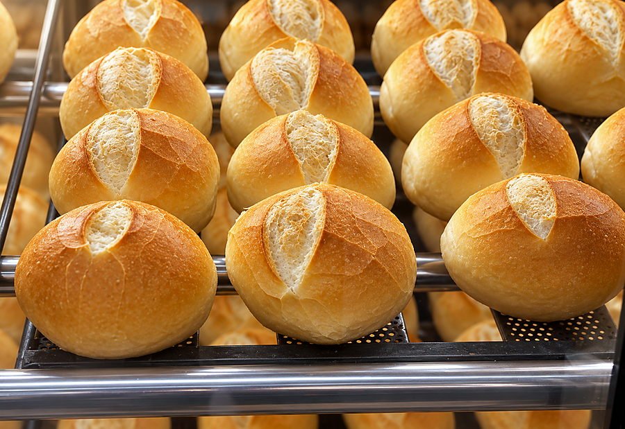 Pães franceses de casca dourada na prateleira da estufa da Bonna Massa